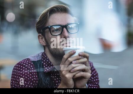 Sad young businessman behind city window drinking takeaway coffee Stock Photo