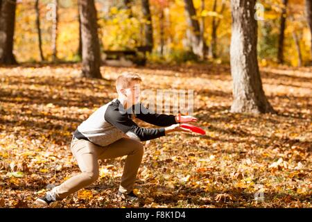 Teenage boy catching flying disc in autumn forest Stock Photo
