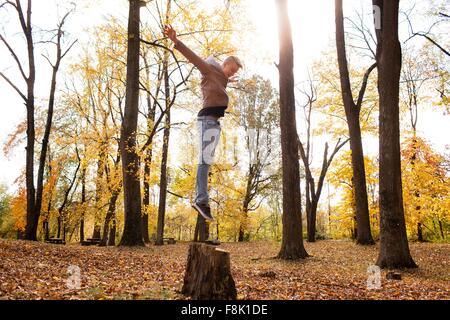 Teenage boy jumping on tree stump in autumn forest Stock Photo