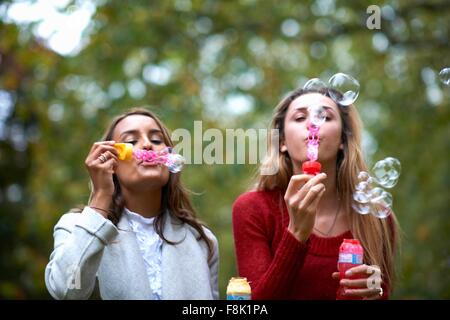 Two young female friends blowing bubbles in park Stock Photo