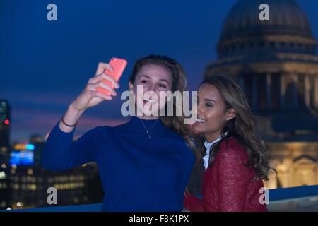 Two young women taking smartphone selfie in front of St Pauls at night, London, UK Stock Photo