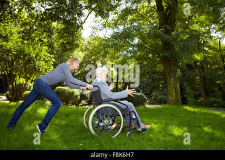 Young woman having difficulties pushing a wheelchair over a meadow Stock Photo