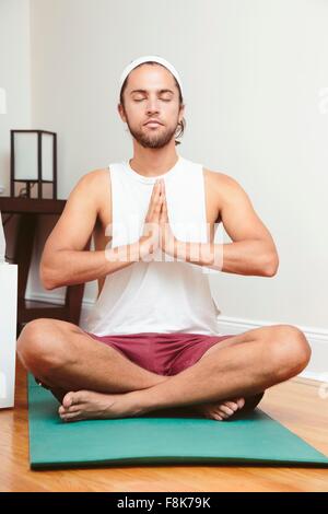 Young man sitting on yoga mat, in lotus position Stock Photo