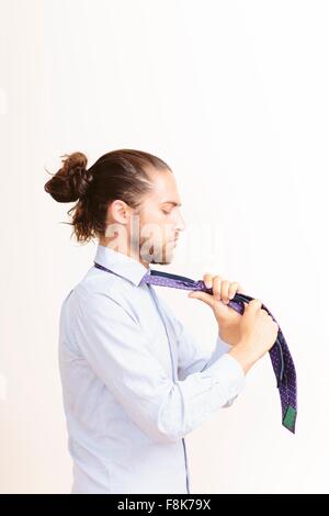 Young man with hair in bun, getting dressed, tying neck tie Stock Photo