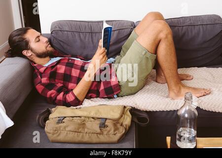 Young man relaxing on sofa, reading book Stock Photo