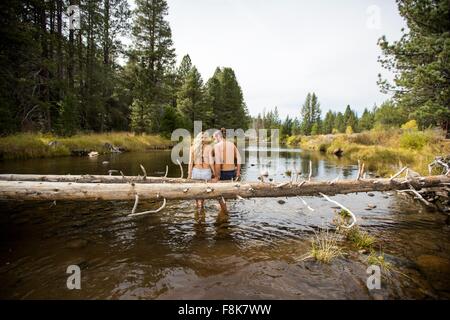 Rear view of romantic young couple sitting on fallen tree in river, Lake Tahoe, Nevada, USA Stock Photo