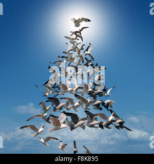 Holiday tree of hope spiritual concept as a group of birds flying in coordinated style shaped as a Christmas tree with the top bird behind a glowing sun as a festive metaphor for winter celebration or fun greeting card. Stock Photo