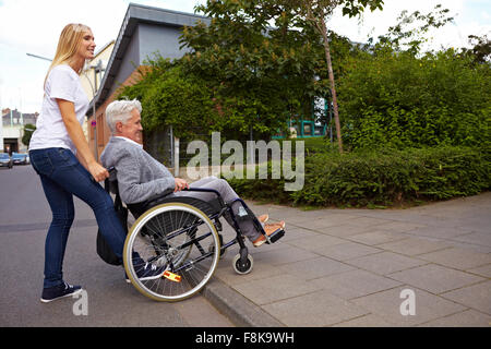 Young woman helping elderly woman in wheelchair over a curbstone Stock Photo