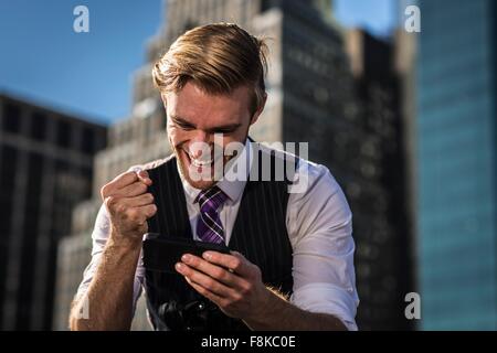 Young businessman in front of office clenching fist at smartphone, New York, USA Stock Photo