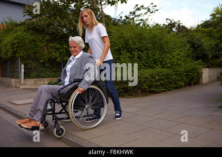 Young woman helping elderly woman in wheelchair over a curbstone Stock Photo