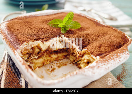 Tiramisu cake in an oven pan on a blue wooden  table with dishes and forks Stock Photo