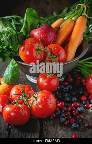 Assortment of fresh fruits, vegetables and berries. Bunch of carrots, spinach, tomatoes and red apples in vintage metal bowl, bl Stock Photo