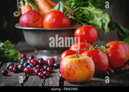 Assortment of fresh fruits, vegetables and berries. Bunch of carrots, spinach, tomatoes and red apples in vintage metal bowl, bl Stock Photo