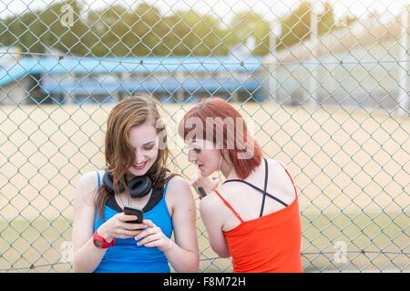 Young women using smartphone beside fence, London, UK Stock Photo
