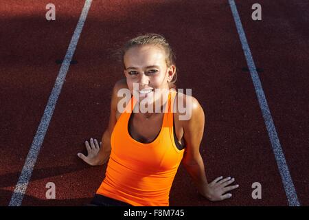 Portrait of young female runner sitting on race track Stock Photo