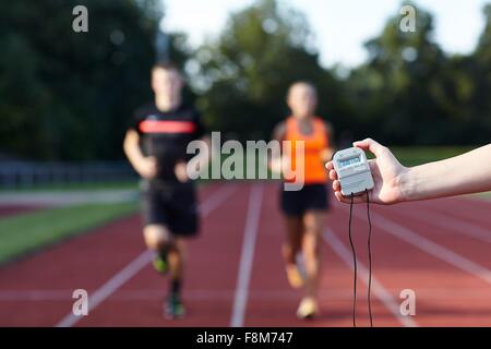 Young man and woman running on race track against stopwatch Stock Photo