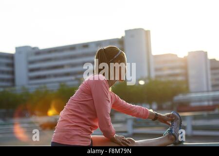 Young female runner touching toes on rooftop Stock Photo