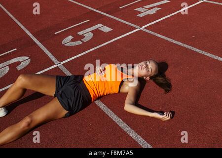 Young female runner lying on back exhausted on race track Stock Photo