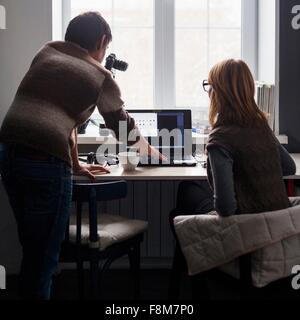 Mid adult man and woman using laptop at desk, rear view Stock Photo