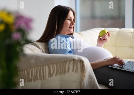 Pregnant woman sitting on sofa, using laptop