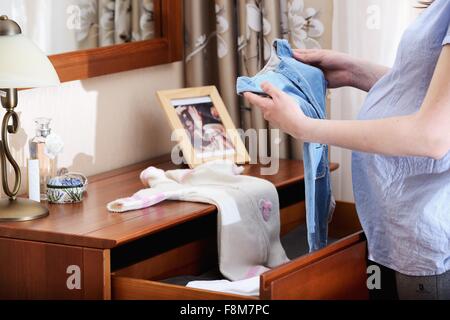 Pregnant woman holding baby clothes, mid section Stock Photo