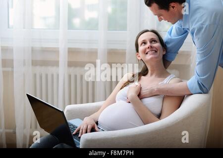Pregnant woman sitting in chair, using laptop, husband holding her hand Stock Photo