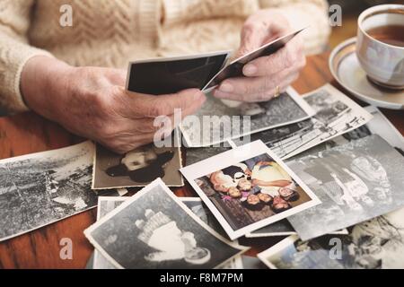 Senior woman sitting at table, looking through old photographs, mid section Stock Photo