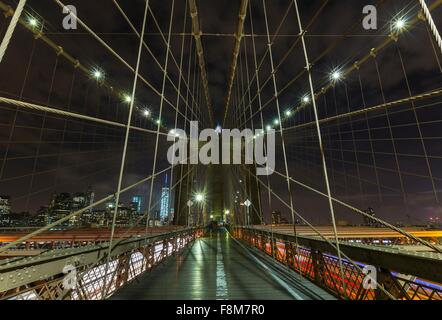 Brooklyn bridge walkway and distant Manhattan financial district skyline at night, New York, USA Stock Photo