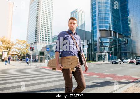 Casual businessman crossing road holding skateboard Stock Photo