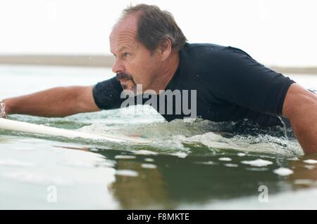 Surfer paddling surfboard out to sea Stock Photo