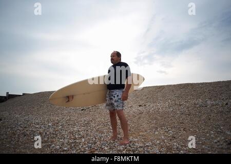 Surfer carrying surfboard on beach Stock Photo