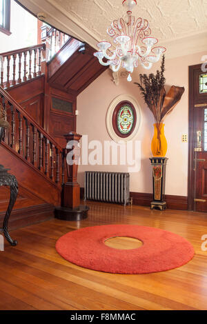 The home of designer Erica Pols. The lobby and fine wooden staircase with a round rug on a polished wooden floor. Victorian traditional style. An oval window and chandelier. Stock Photo