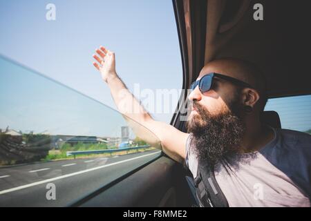 Bearded man sticking hand out of car window on highway, Garda, Italy Stock Photo