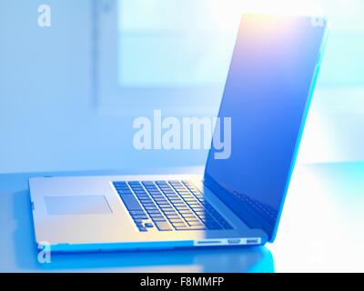 Side view of open laptop on desk, sunlight coming through window Stock Photo