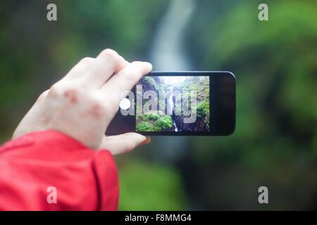 Womans hand holding smartphone, photographing Aira Force waterfall, Penrith, Cumbria, UK Stock Photo