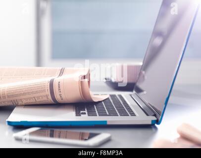 Reviewing financial affairs with newspaper market data page sitting on a laptop computer Stock Photo