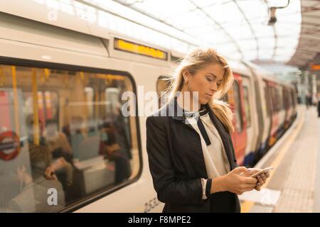 Business woman texting on platform, Underground station, London, UK Stock Photo