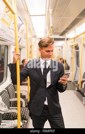 Businessman texting on tube, London Underground, UK