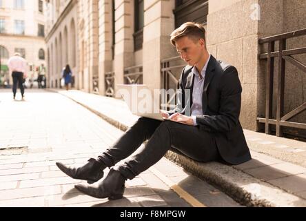 Businessman using laptop on kerb, London, UK Stock Photo