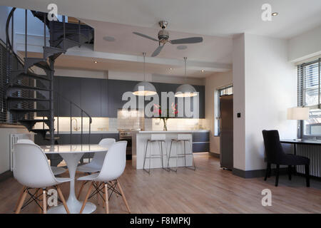 Wide angle of living space and kitchen with spiral staircase. Lights on Stock Photo