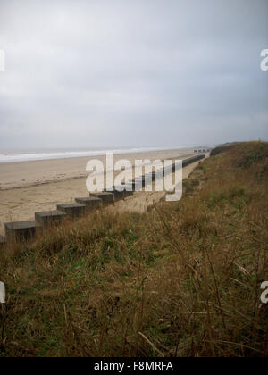 World War Two concrete tank traps on the east coast of England. In a straight line on the edge of the beach. Blue sky with white clouds as background. Stock Photo