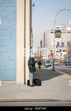 A man standing on the corner of the West 40th street and 11th Avenue and lighting a cigarette in Manhattan Stock Photo