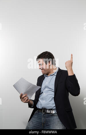 Dark-haired european businessmann is dancing full of delight with his left index finger into the air and a piece of paper in his Stock Photo