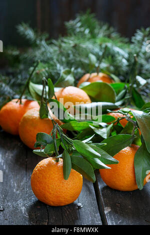 Tangerines with leaves with Christmas tree over old wooden table. Natural day light. Dark rustic style Stock Photo