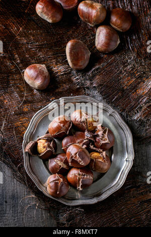 Heap of grilled edible chestnuts in vintage metal plate over dark palm crust. Top view
