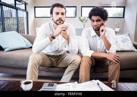 Worried gay couple with bills on table looking at camera Stock Photo