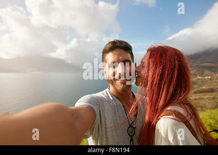 Young couple taking a selfie outdoors. POV shot man holding a camera and taking a self portrait with woman kissing him. Stock Photo