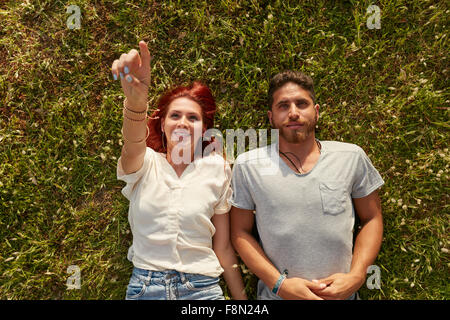 Overhead view of young man and woman lying on the grass, with woman pointing at something interesting. Top view of relaxed young Stock Photo