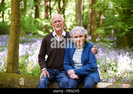 Senior Couple Sitting On Log In Bluebell Wood Stock Photo