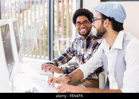 Smiling gay couple talking while working on computers Stock Photo